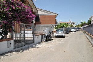 Una strada residenziale con auto parcheggiate e uno scooter, un cancello e un edificio con facciata in mattoni.