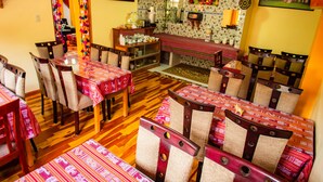 A dining area with wooden tables and chairs, a bench, and a kitchen area in the background. - Intitambo Three Star Hotel With Panoramic View of the Mountains (Ollantaytambo)
