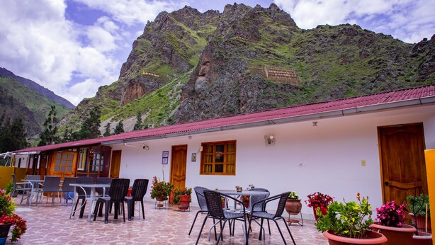 A building with a red roof and white walls, outdoor seating with chairs and tables, and potted plants. - Intitambo Three Star Hotel With Panoramic View of the Mountains (Ollantaytambo)