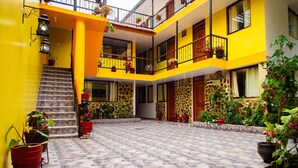 A multi-level building with yellow walls, a tiled courtyard, and multiple balconies with potted plants. - Intitambo Three Star Hotel With Panoramic View of the Mountains (Ollantaytambo)