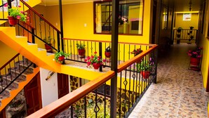 A multi-level interior with yellow walls, a staircase with wooden railings, and potted plants. - Intitambo Three Star Hotel With Panoramic View of the Mountains (Ollantaytambo)