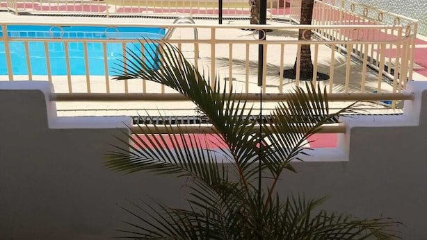 A pool area with a white fence, a palm tree, and a building with large windows in the background. - Room-roommate for Rent in Flic en Flac (Black River)