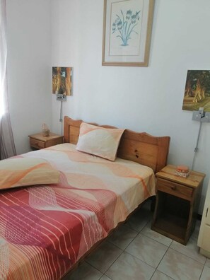 A bedroom with a wooden bed, a nightstand, a bedside table, and two wall-mounted paintings. - Room-roommate for Rent in Flic en Flac (Black River)