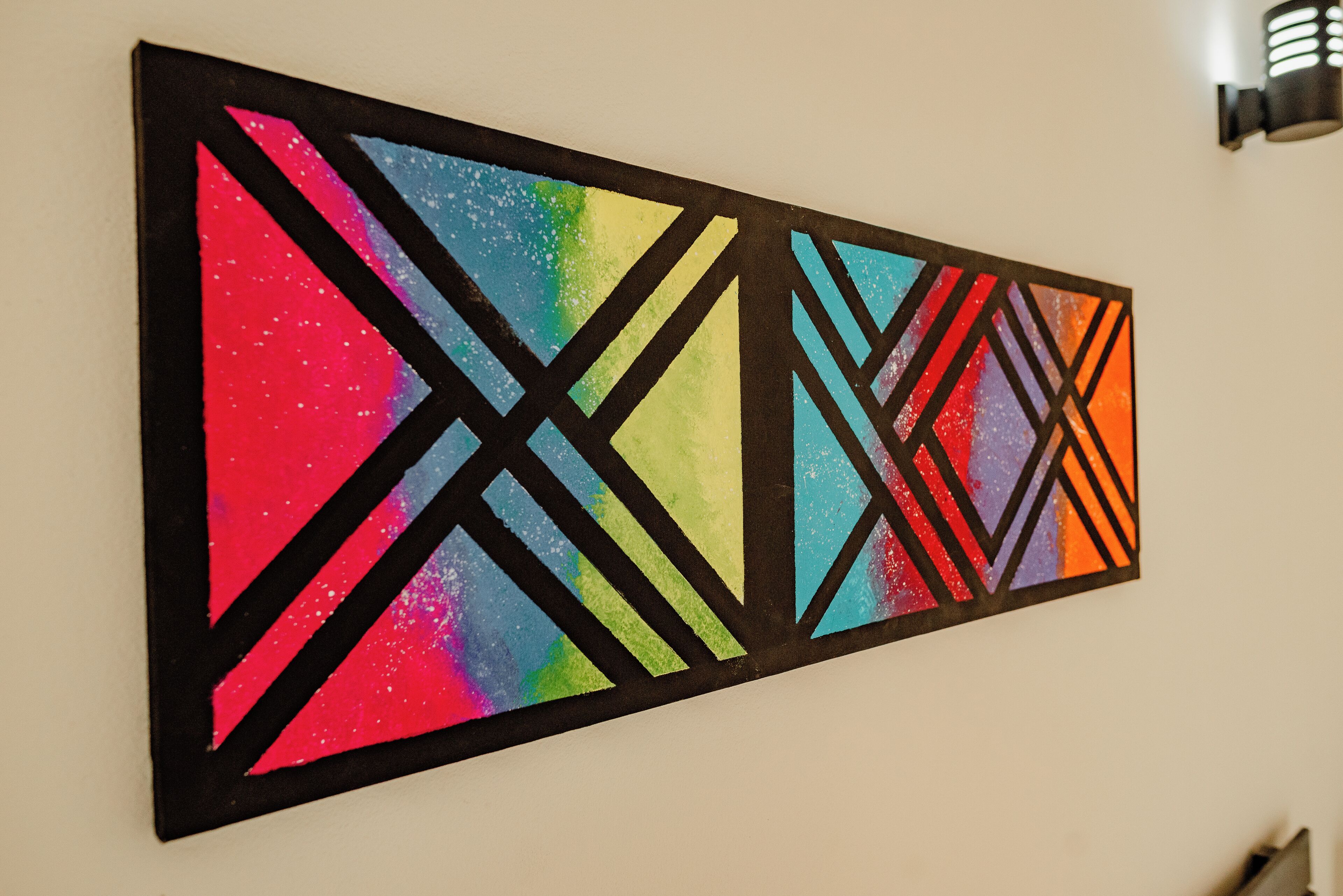 Un quadro astratto e colorato con motivi geometrici su una parete bianca.