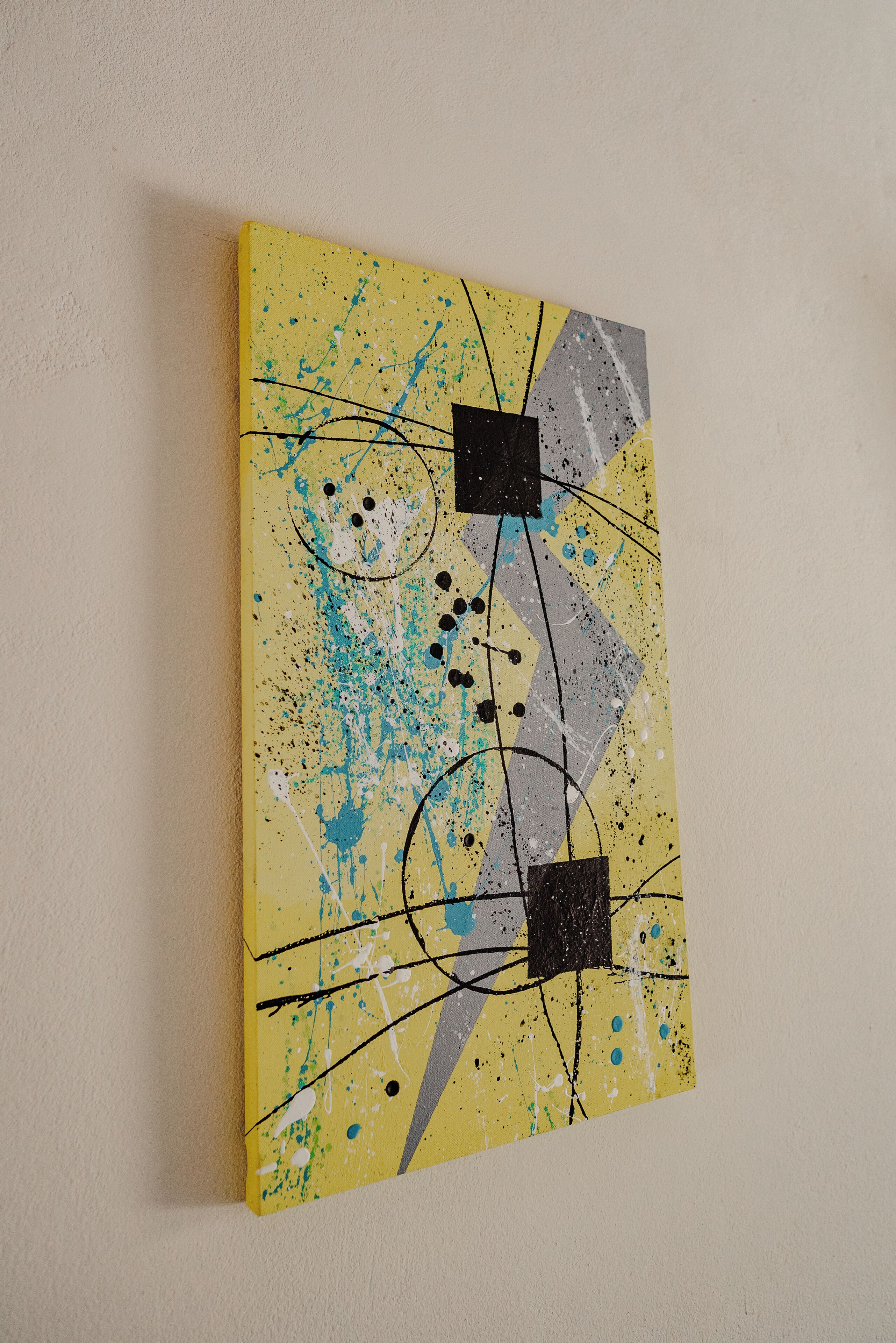 Een gele abstracte schildering met spatjes en lijnen op een muur.