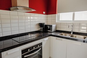 A kitchen with white cabinets, a black countertop, a coffee maker, a microwave, and a stainless steel sink.