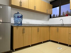 Una cocina con armarios de madera, un refrigerador de acero inoxidable, un dispensador de agua y una ventana con vistas a árboles.