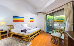 A hotel room with a bed, a desk, a chair, and a view of greenery through the window.