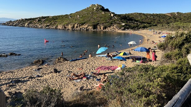 A beach with people swimming and sunbathing, umbrellas, and a rocky hill in the background. - Villa a few Steps From the Beach (Santa Teresa di Gallura)