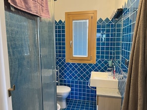 A bathroom with a shower, toilet, and sink, featuring blue tiles and a wooden window frame.