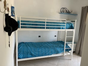 A bunk bed with a blue striped mattress, a shelf with two tennis rackets, and a wall-mounted coat rack with a black jacket.