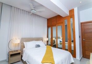 Habitación de hotel con cama, mesita de noche, lámpara, ventilador de techo y armario de madera.