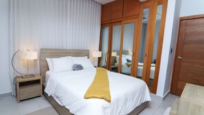 Una habitación de hotel ordenada con una cama grande, cabecera de madera y un armario con puertas espejadas.