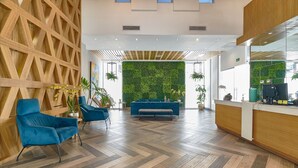 Un vestíbulo moderno con un muro de madera, asientos azules, un muro verde con plantas y un mostrador de recepción.
