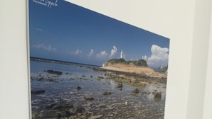 A photograph of a coastal scene with a lighthouse, displayed on a white wall above a white bed. - The Home of Athena Paestum (Capaccio-Paestum)