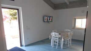 A dining area with a table and chairs, a television on the wall, and a window with blinds. - The Home of Athena Paestum (Capaccio-Paestum)