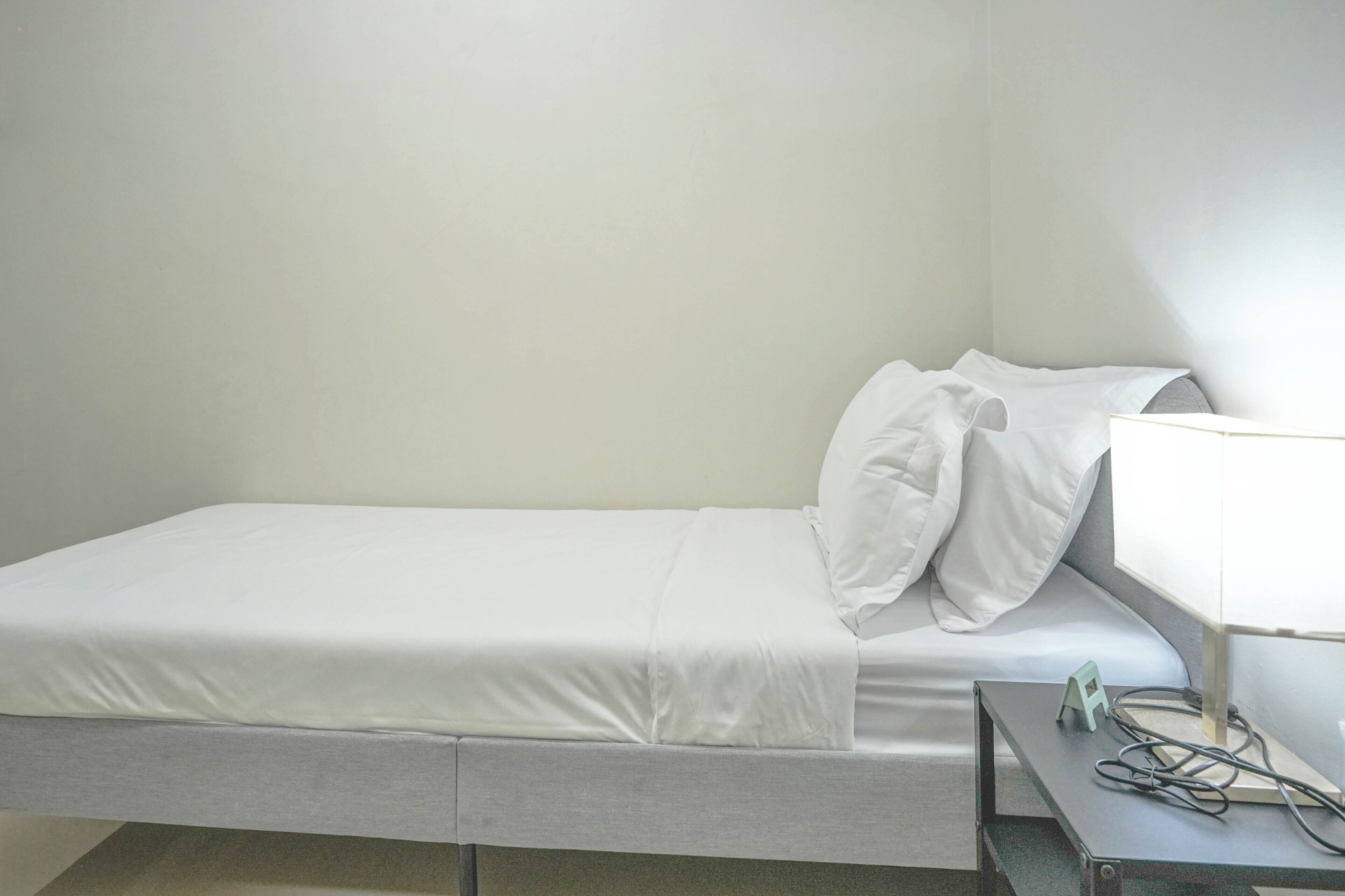 A single bed with white bedding, a bedside table with a lamp, and a power outlet.