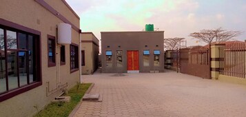 Un edificio con un paseo empedrado, una puerta roja y una zona vallada.