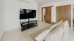 A modern living room with a flat-screen TV on a stand, a sofa with cushions, and a wooden wardrobe. - Spectacular Beach And Mountain View Condo - 5 Min From The Beach (Puerto Vallarta)