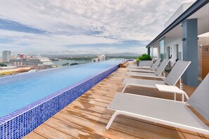 An infinity pool with a wooden deck and lounge chairs, overlooking a cityscape and a cruise ship. - Spectacular Beach And Mountain View Condo - 5 Min From The Beach (Puerto Vallarta)