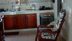 A kitchen with wooden cabinets, a stove, and a chair with a patterned cushion. - Room in Guest Room - Green Sea Villa Helen Inn, Kilometer 4 Circunvalar (San Andrés)