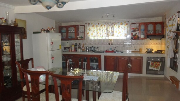 A kitchen with wooden cabinets, a glass dining table, and chairs. There is a refrigerator, a stove, and various kitchen utensils. - Room in Guest Room - Green Sea Villa Helen Inn, Kilometer 4 Circunvalar (San Andrés)