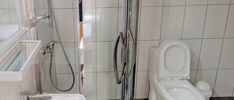 A bathroom with a shower, toilet, sink, and a glass-enclosed shower area.