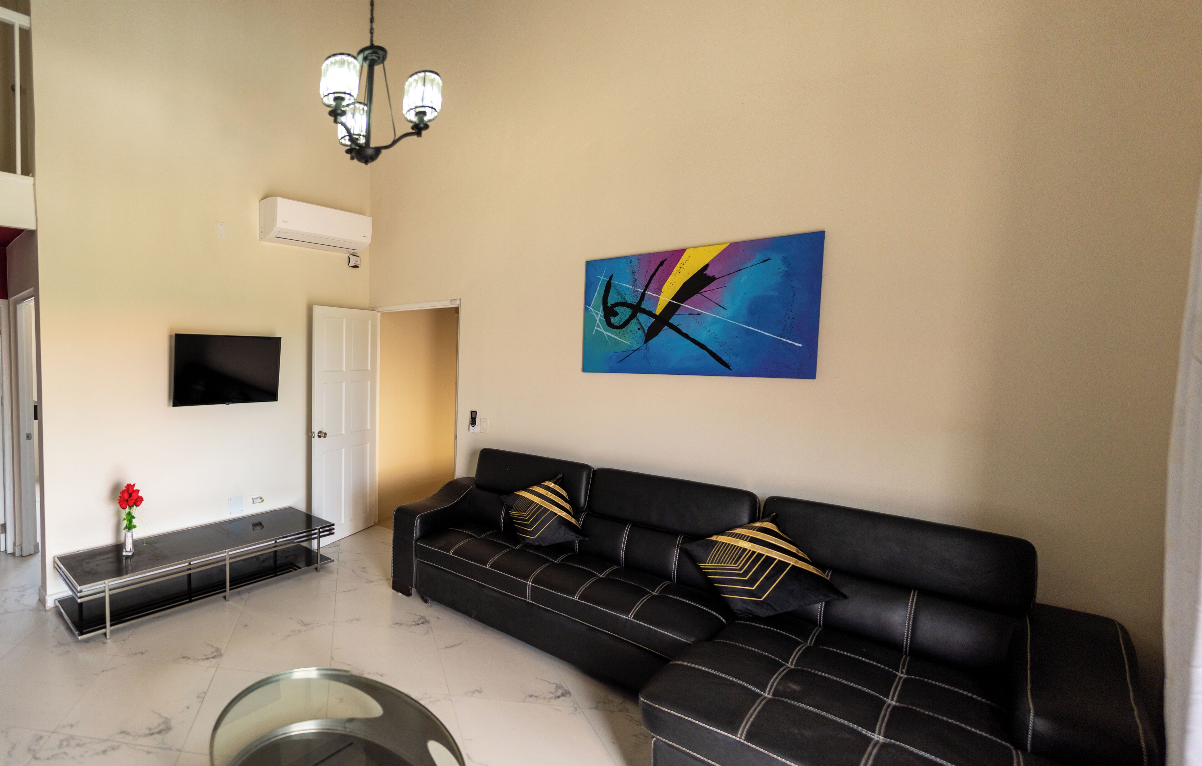 Un salon moderne avec un canapé en cuir noir, une table basse en verre et un tableau abstrait aux couleurs vives accroché au mur.