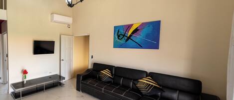 Un salon moderne avec un canapé en cuir noir, une table basse en verre et un tableau abstrait aux couleurs vives accroché au mur.