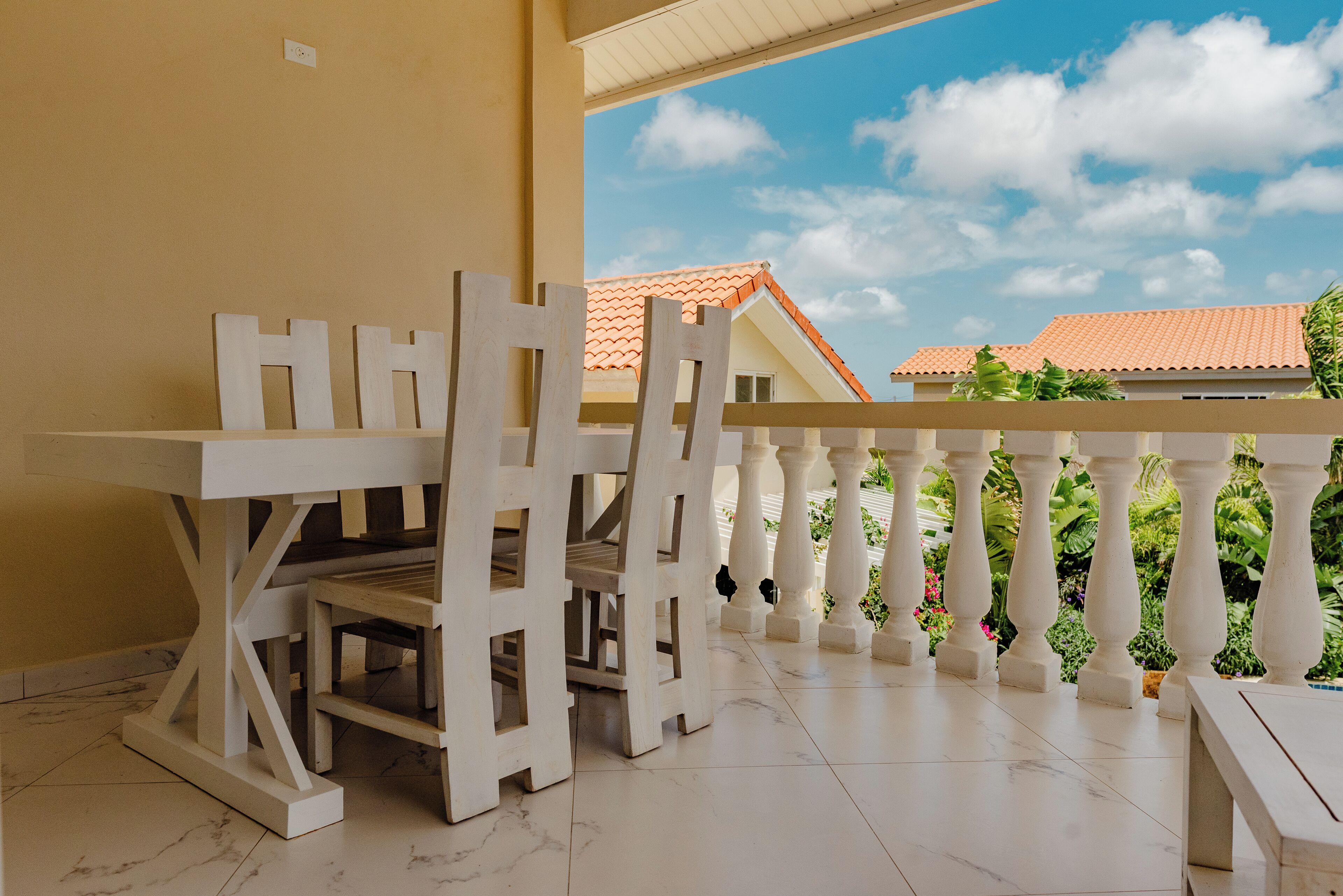A balcony with white wooden furniture, including a table and chairs, and a view of a building with a red roof.