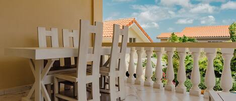 A balcony with white wooden furniture, including a table and chairs, and a view of a building with a red roof.