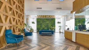 A modern lobby with a wooden wall, blue seating, a green wall with plants, and a reception desk. - Apartamento N1401 - Downtown Santo Domingo (Santo Domingo)