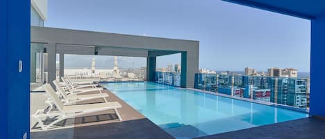 Ein Pool auf dem Dach mit Liegestühlen, freier Blick auf den Stadtpanoramahimmel und moderne Architektur.