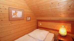 Acogedora habitación de cabaña de madera con una cama, un cuadro de un ciervo enmarco y un farol encendido.