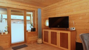 Una habitación con paneles de madera, un vidrio corredero, un televisor de pantalla plana sobre un mueble de madera y una mesita con adornos.