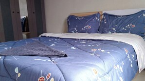 Un lit avec une couvre-lit à motifs floraux bleus et des coussins assortis, un coussin blanc et un plaid gris.