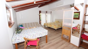A cozy room with a wooden ceiling, a bed with a colorful bedspread, a small table with a floral tablecloth, and a chair with a red cushion. - Rovinj-home Studio (Rovinj)