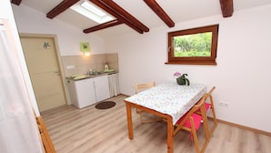 A compact kitchen with a dining area, wooden beams on the ceiling, a window with a view of greenery, and a small table with a floral tablecloth. - Rovinj-home Studio (Rovinj)