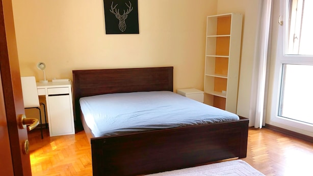 Een slaapkamer met een houten bed, een bureau, een stoel, een witte kledingkast en een raam.