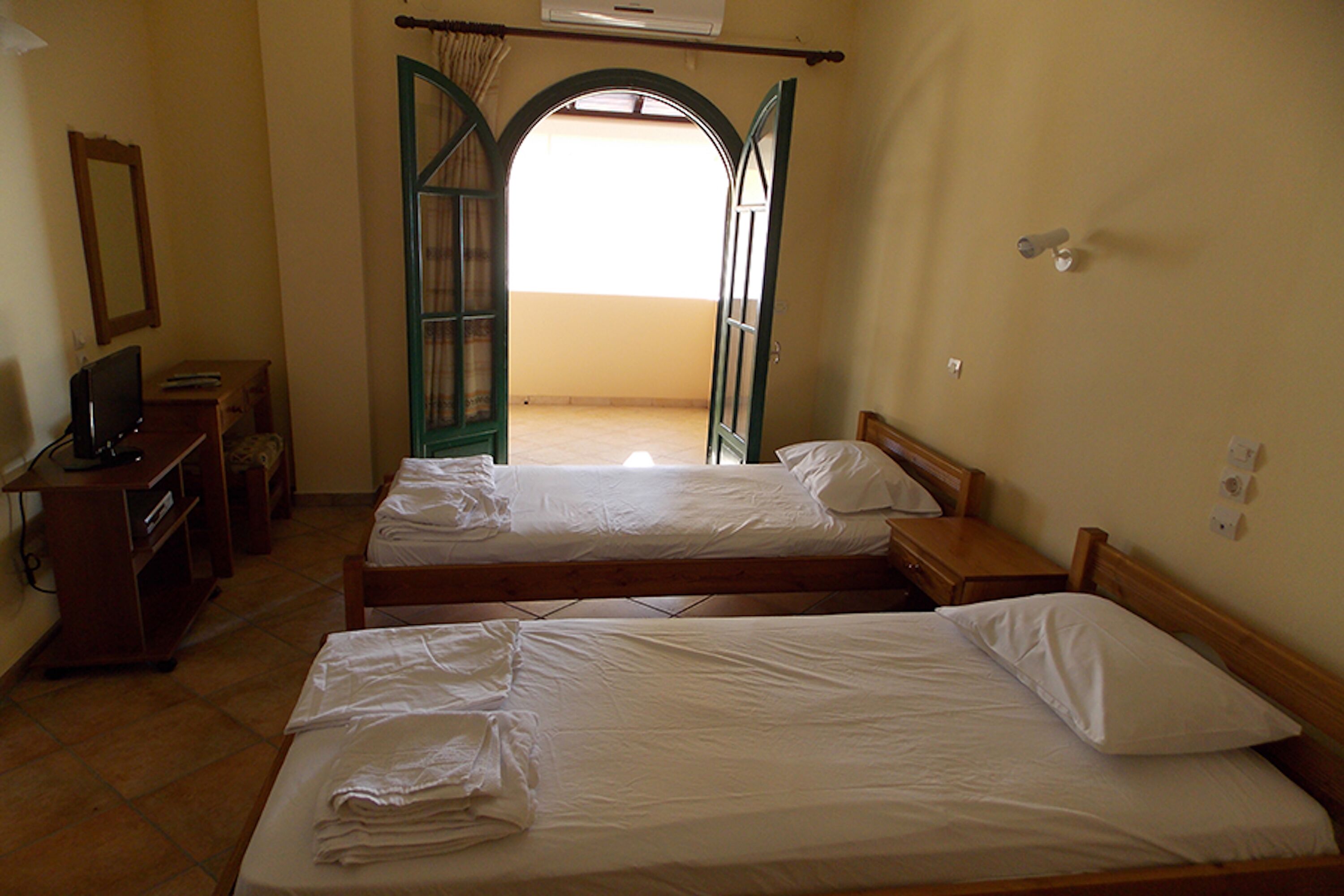 Habitación con dos camas, un escritorio, una silla y una puerta abierta que da a un balcón.