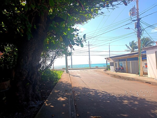 A coastal road with a sidewalk, a building with a motorcycle parked outside, and a view of the sea.