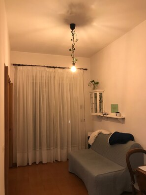 A bedroom with a bed, a chair, a bedside table, a hanging plant, and a window with curtains. - The Sweet Frascati Home (Monte Porzio Catone)