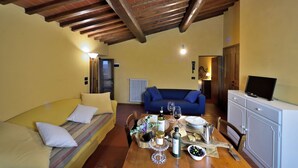 A cozy living room with a yellow sofa, a blue couch, and a wooden table set with wine glasses, bottles, and a small bowl of olives. - Il Bellini - Tuscany Farmholiday (Castelfranco Piandisco)