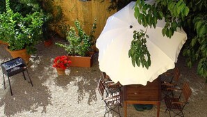 An outdoor patio with a wooden table and chairs, surrounded by potted plants and a white umbrella providing shade. - Il Bellini - Tuscany Farmholiday (Castelfranco Piandisco)