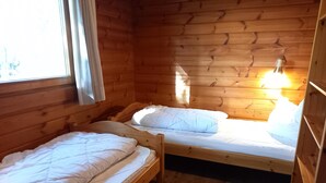 Una cabaña con dos camas litera de madera, una ventana con cortinas y un aplique de pared.