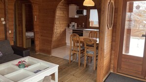 Acogedor interior de cabaña con comedor, cocina y una pequeña zona de estar.