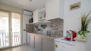 Una cocina moderna con microondas integrado, cafetera y refrigerador pequeño. Hay una ventana con persianas, un balcón y un salpicadero de azulejos.