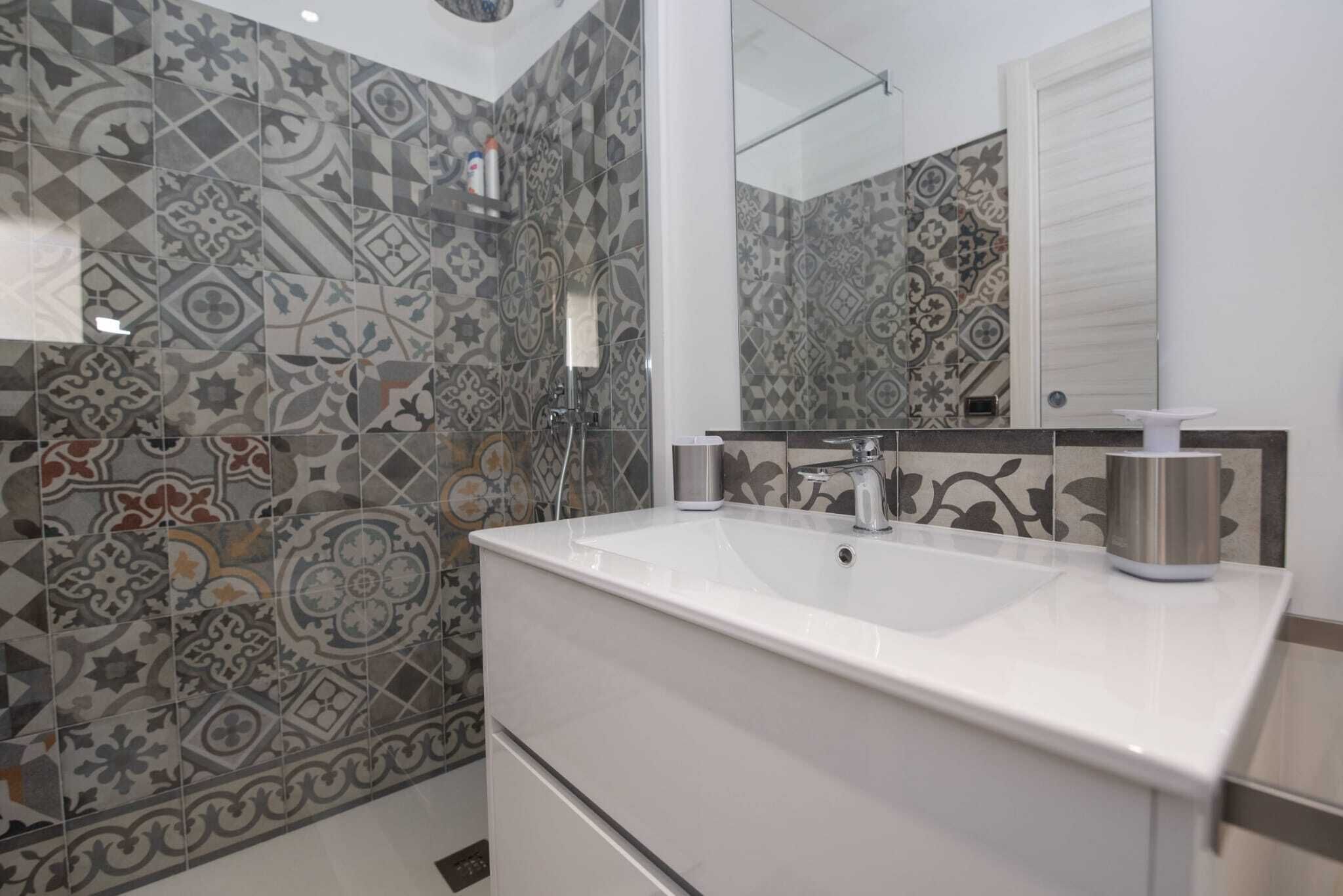 A bathroom with patterned tiles, a white sink, a mirror, and a shower.