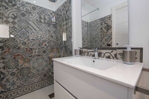 A bathroom with patterned tiles, a white sink, a mirror, and a shower.