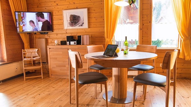 A wooden interior with a round dining table, chairs, a laptop, a television, and a window with curtains. - Come to This House to Stay for Holidays (Oberharz am Brocken)